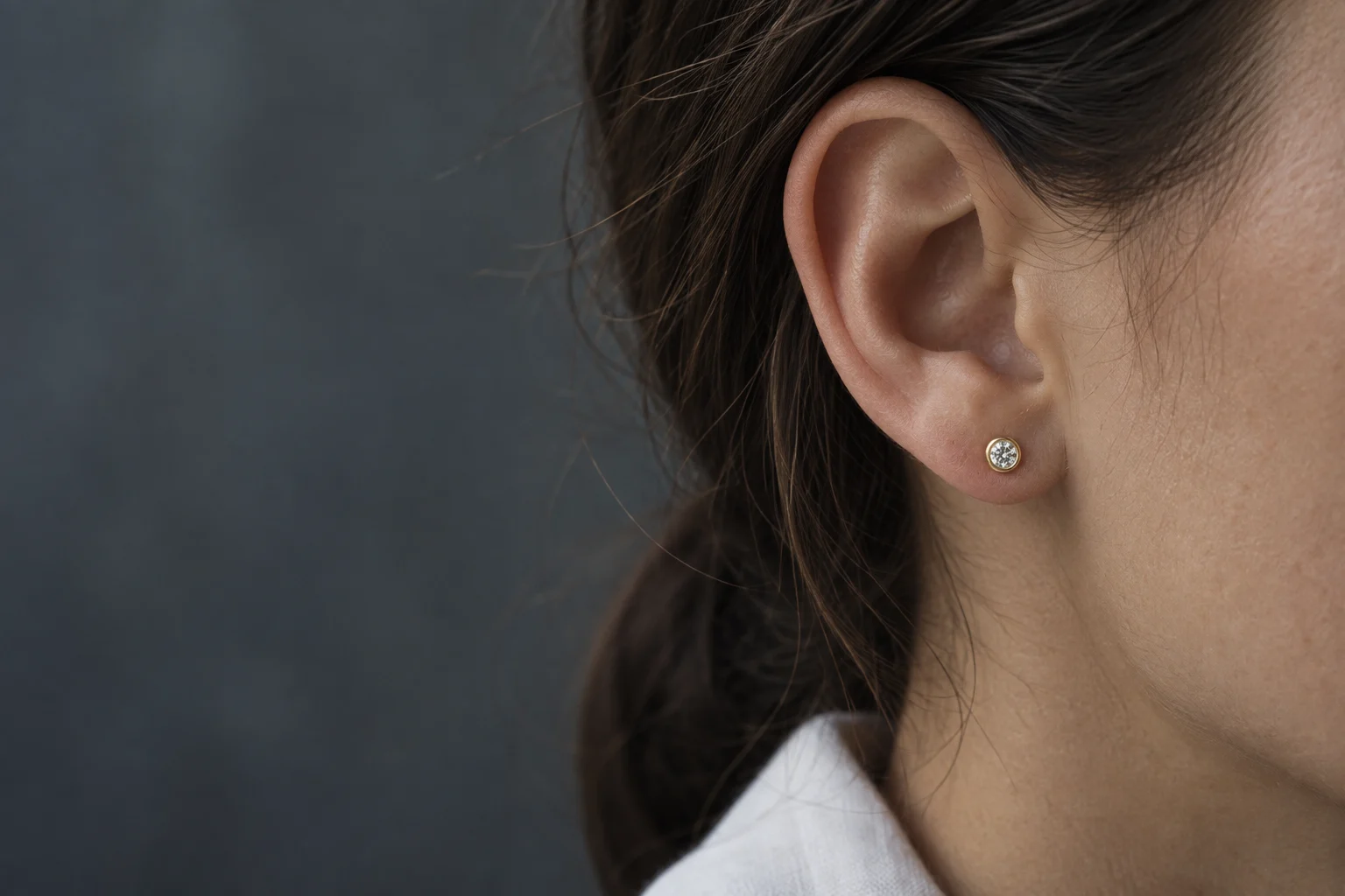 Illustrative close-up of a small gold bezel stud worn on an earlobe
